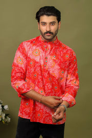 Man wearing a red Bandhani printed kurta shirt with black jeans against an olive green background.